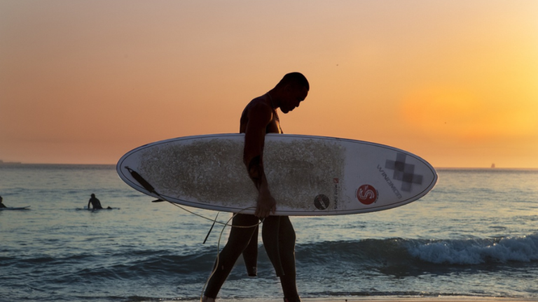 surfers walking with shortboard at sunset